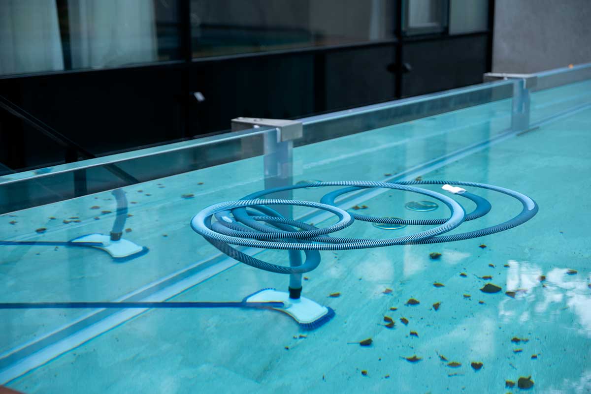 Scopa per la pulizia immersa nell'acqua della piscina esterna, per pulire il fondo e le pareti, piscina piena di foglie e altri segni di incuria - sporco
