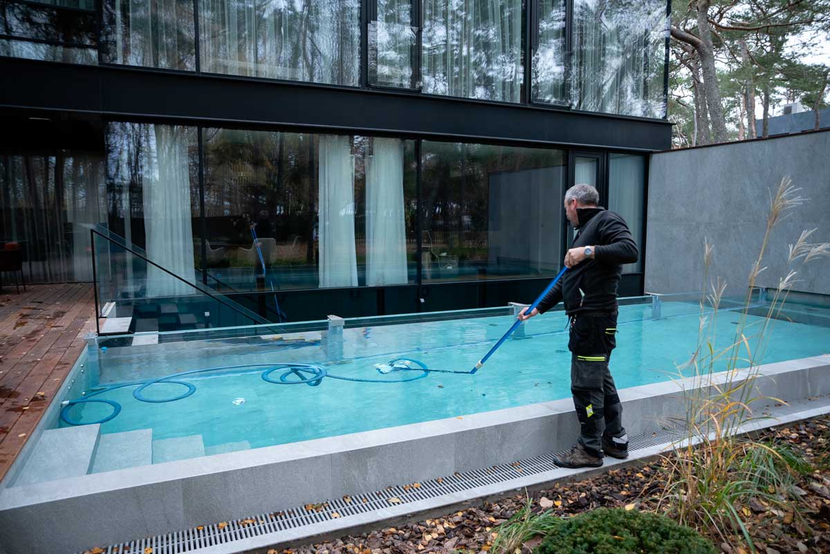 Piscina all'aperto con acqua torbida e sporca, macchie marroni e sporcizia visibili sulla superficie, una persona in piedi accanto alla piscina.