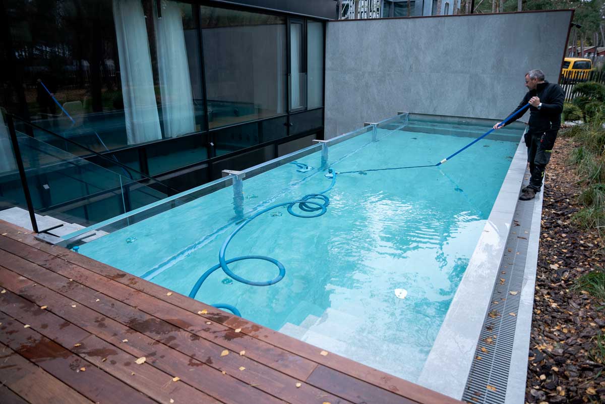 Una piscina con acqua verde chiaro e torbida, la superficie ricoperta da uno strato di alghe, una situazione immortalata mentre una persona pulisce la piscina.