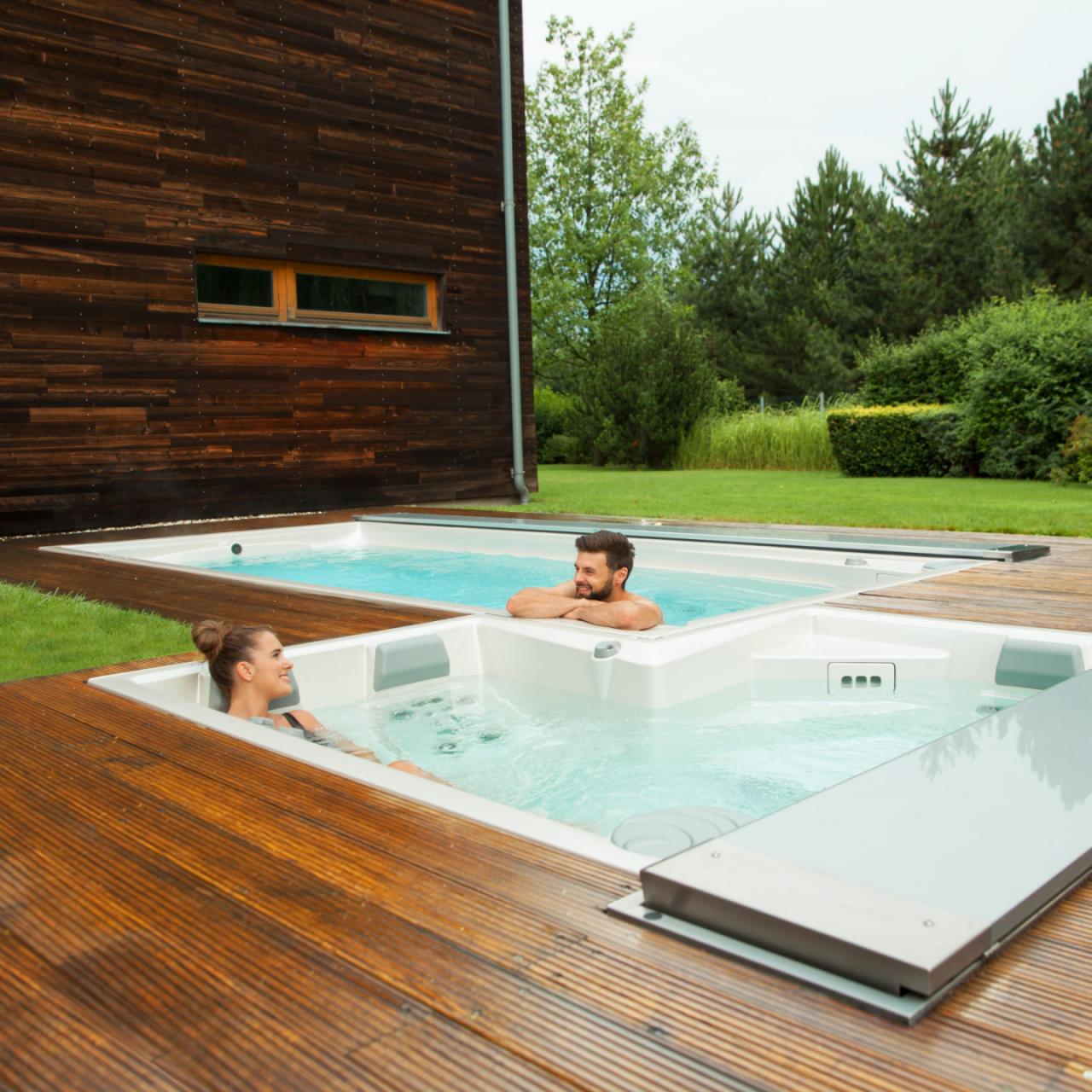 Coppia si rilassa nelle piscine all'aperto USSPA, dotate di vasca idromassaggio e sistema di nuoto controcorrente, installate su una terrazza in legno.