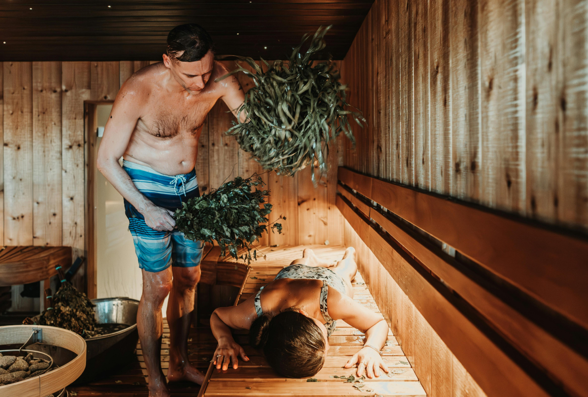 Un uomo sta frustando una donna con una frusta di betulla nella sauna: un rituale tradizionale della sauna per il rilassamento.